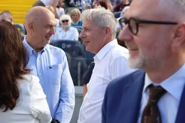 Trzech mężczyzn rozmawia na trybunach podczas plenerowego wydarzenia publicznego.